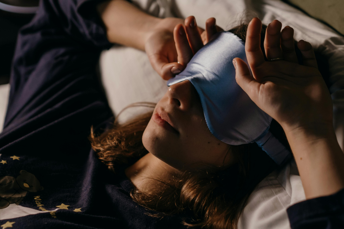 Mulher a dormir com máscara de olhos numa divisão escura, representando práticas saudáveis para bloquear a luz