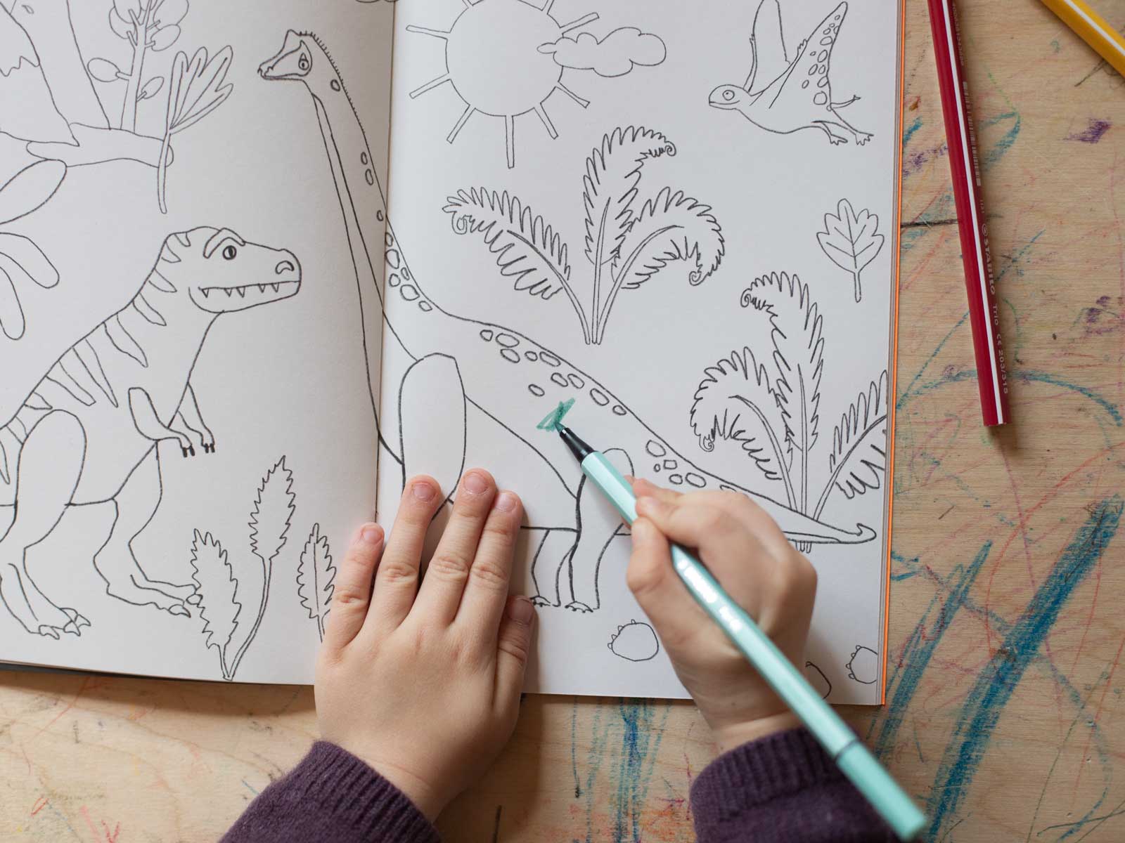 Kind malt im Halfbird Krummtier to go-Heft Dinosaurier aus