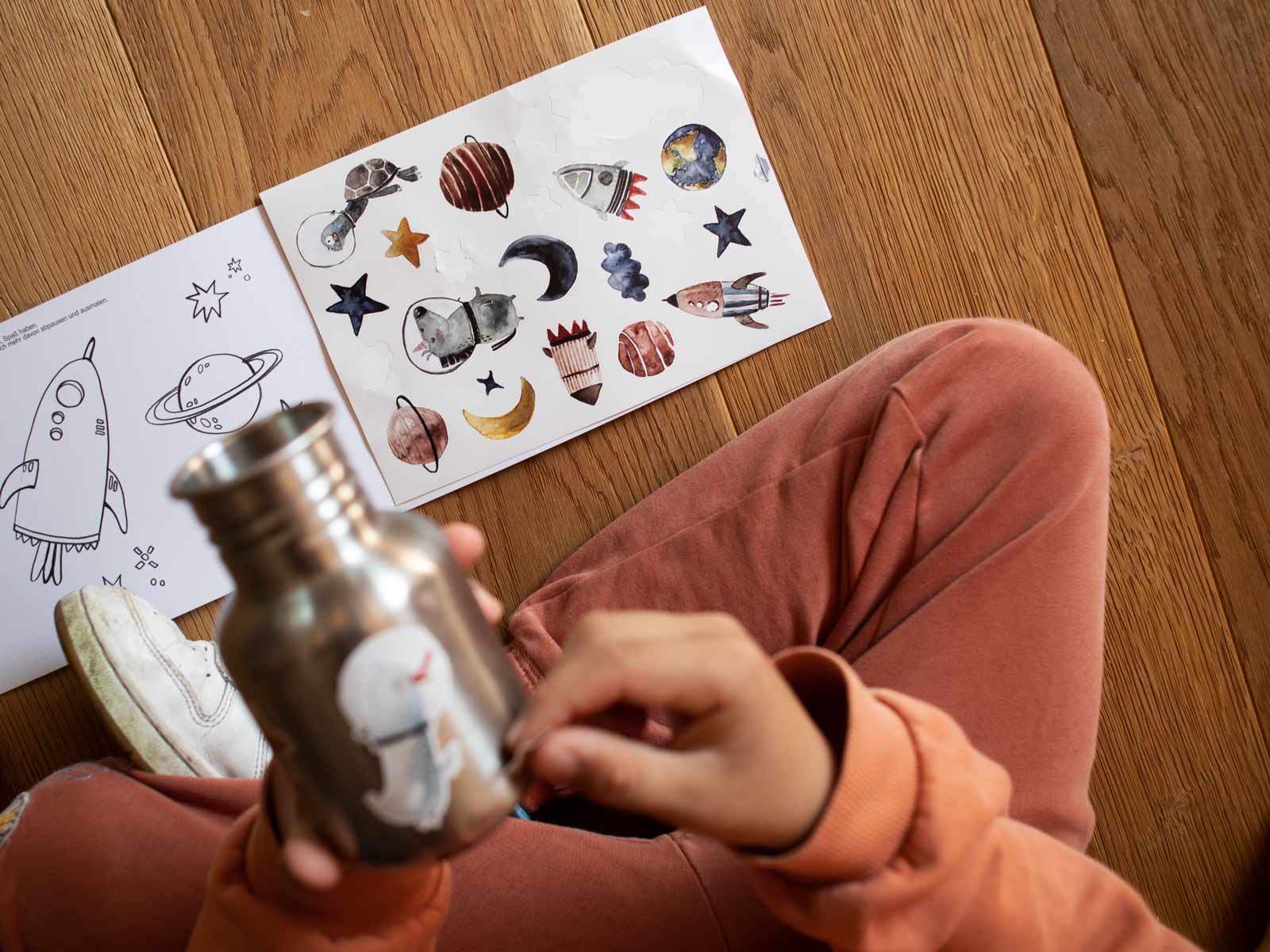 Kind beklebt Edelstahl Trinkflasche mit den spülmschinenfesten Stickern von Halfbird