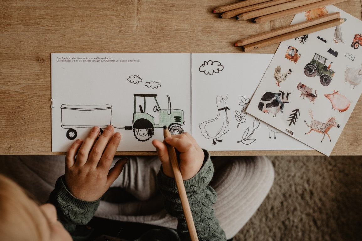 Kind malt mit buntstiften einen Traktor aus daneben liegen sspülmaschinenfeste sticker und stifte von halfbird
