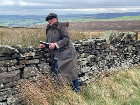 Artist Ashley Jackson leaning against a dry stone wall on the open moorland above Holmfirth 