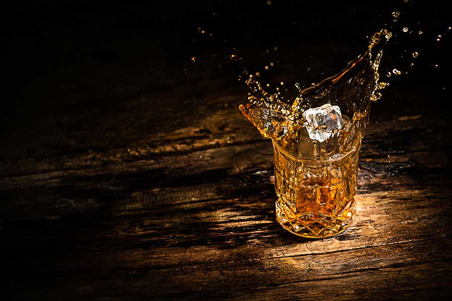 A glass of whiskey with splashes from the ice cube