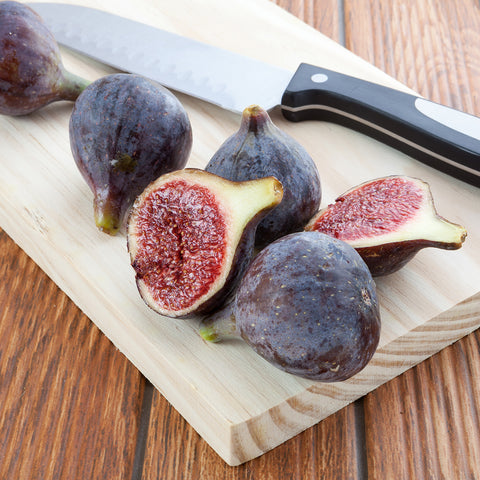 Black Mission Fig cut open on wooden cutting board with knife