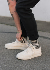 A model wears black and white striped hemp socks, with white sneakers and black trousers