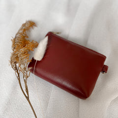A red cactus leather zip wallet sits on a white fabric background with dried flowers