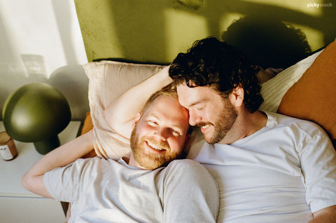 Two men in a loving embrace, lie on bed. 