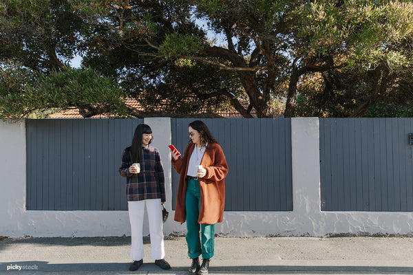 Two young ladies, Japanese and Māori, walk the street of Christchurch. Laughing with their phones out.