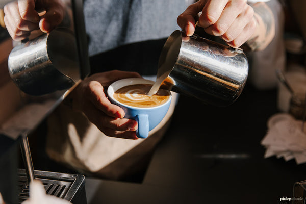 Close up of barista pouring frothed milk into a light blue coffee cup.