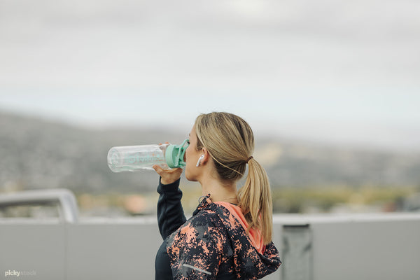 Blonde lady in early thirties drinks from water bottle. We see her from profile.