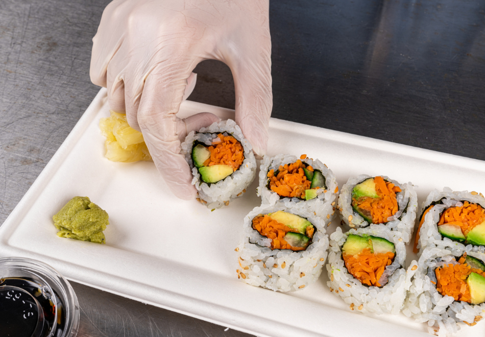 person wearing disposable gloves and placing sushi on a rectangular molded fiber plate