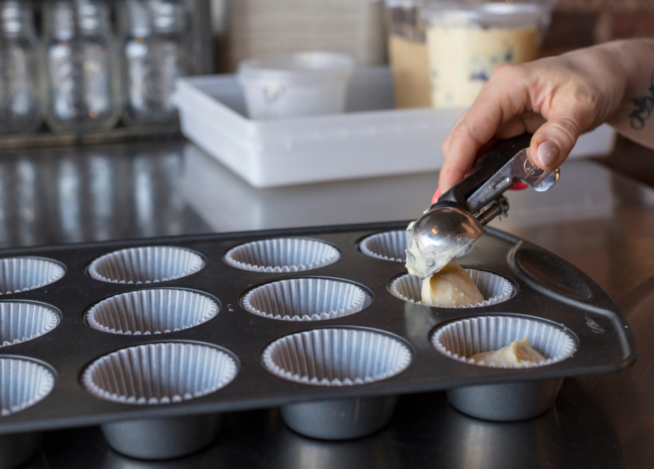 person scooping cupcake batter into lined muffin pan