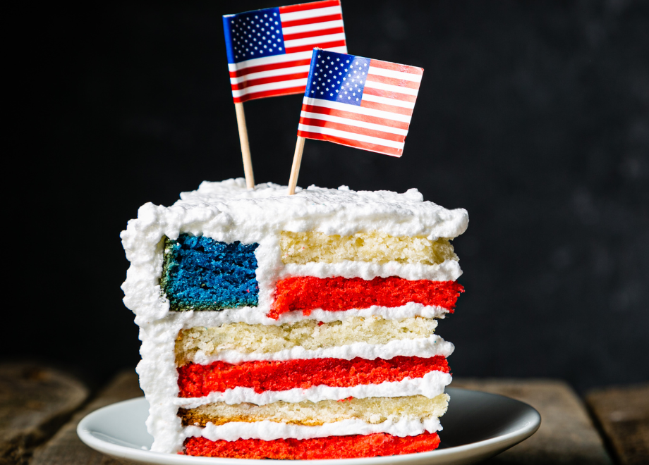 a slice of cake made to look like the American flag inside. there is an American flag atop the cake