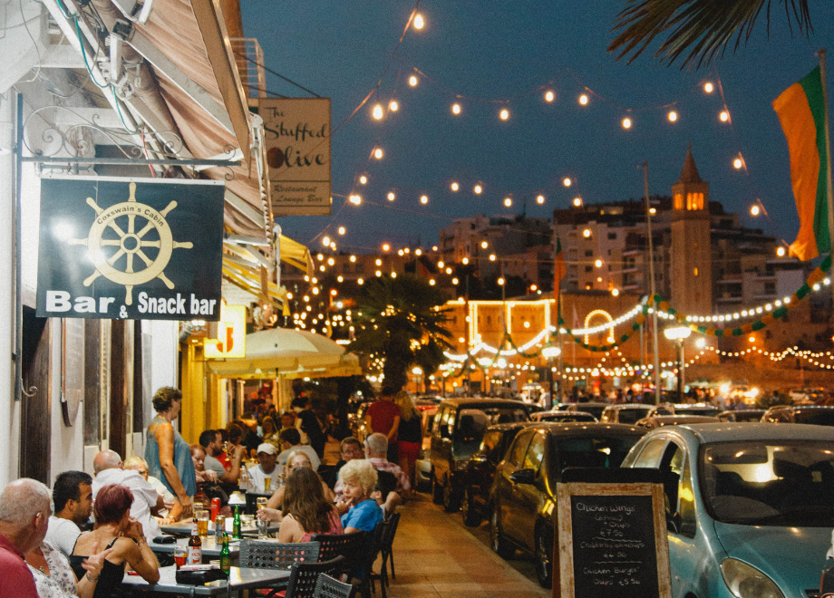 a busy sidewalk bar at night in a warm climate in the evening