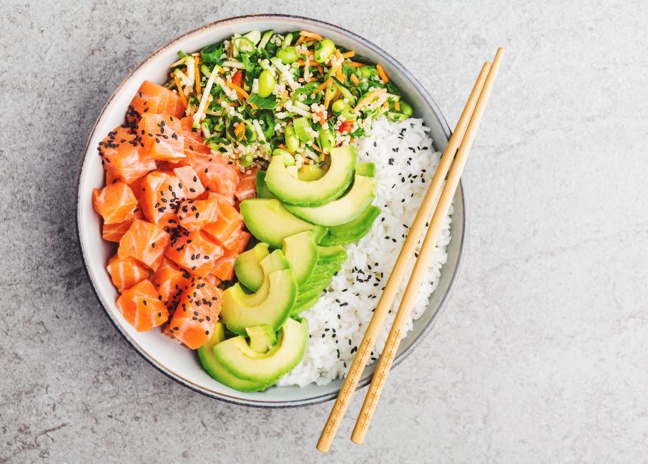 poke bowl with sushi rice, raw salmon, sliced avocado, and seaweed slaw with green onion and edamame. there is a pair of chopsticks resting on the bowl