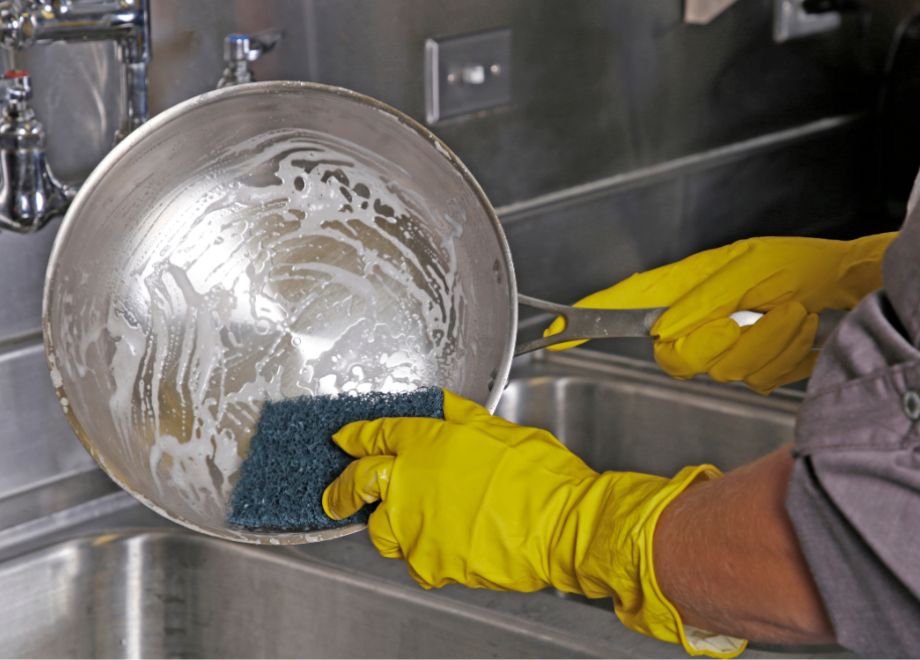 person wearing yellow rubber glove and cleaning a bowl with a scouring pad