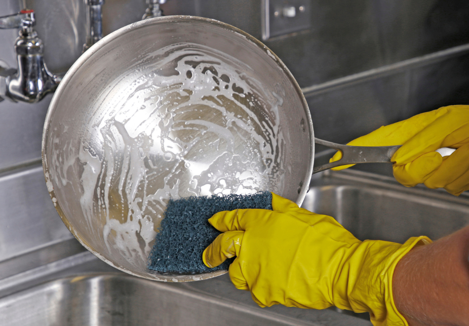 person wearing yellow latex gloves and scouring a pot