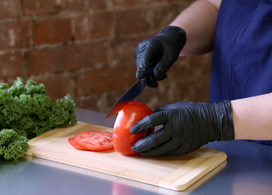 person wearing black nitrile gloves and slicing tomatoes