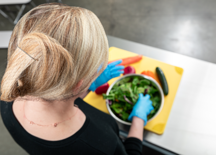 kitchen worker wearing a hairnet and prepping a salad