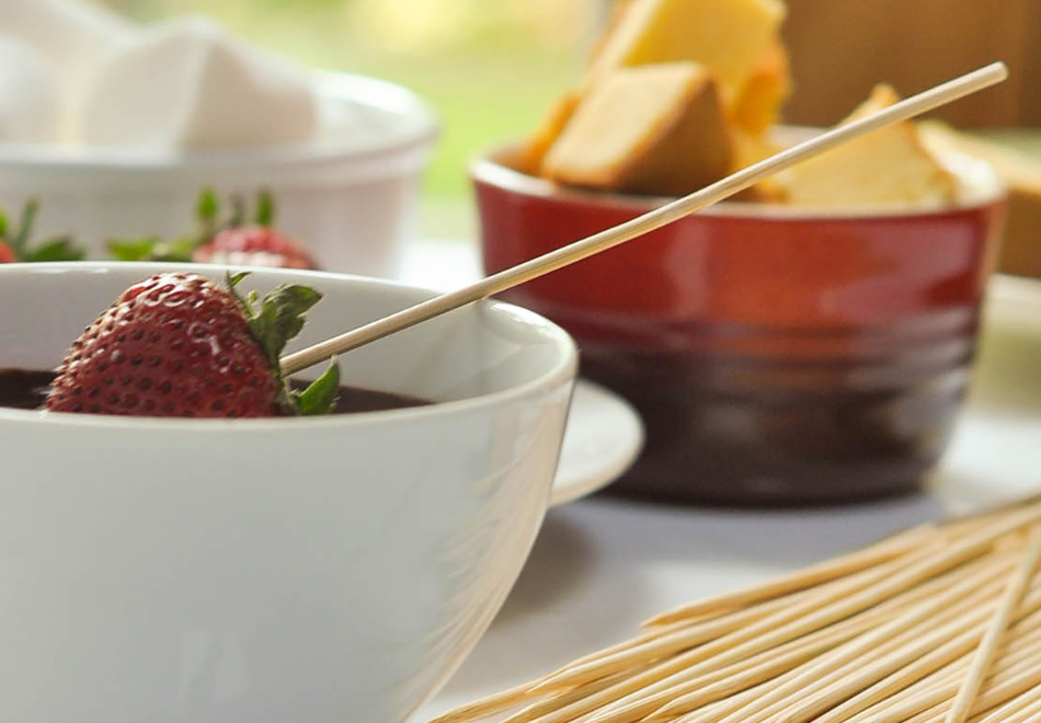 bamboo skewers being used to dip strawberries in chocolate