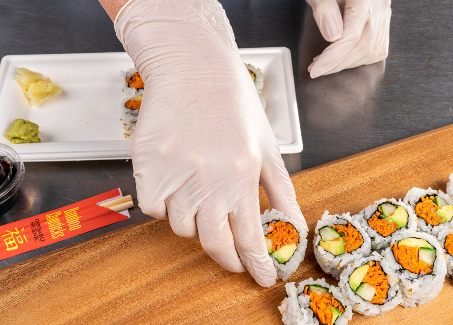 Person wearing hybrid gloves and plating fresh sushi on a primeware 10" x 5" rectangular molded fiber plate