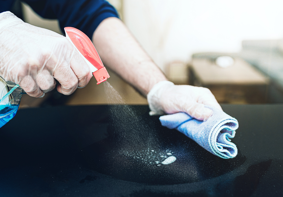 person wearing disposable gloves and cleaning a stovetop with a towel