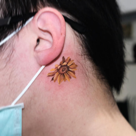 Microrealistic sunflower tattooed behind the ear