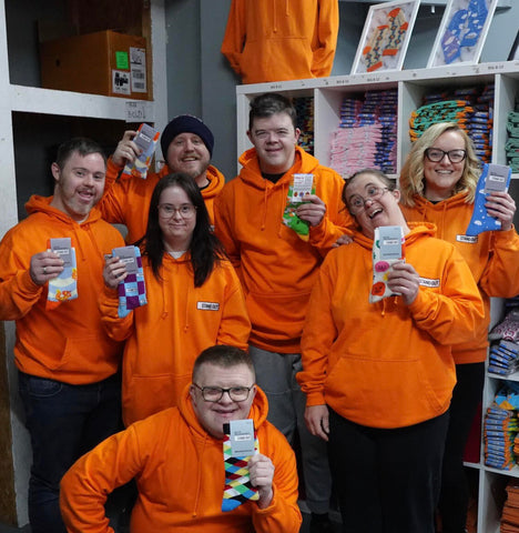7 people with orange hoodies holding socks and smiling