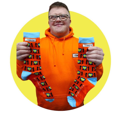 man smiling and holding a pair of colourful socks with the number 21 mirrored to create 3 hearts in the middle for world down syndrome day