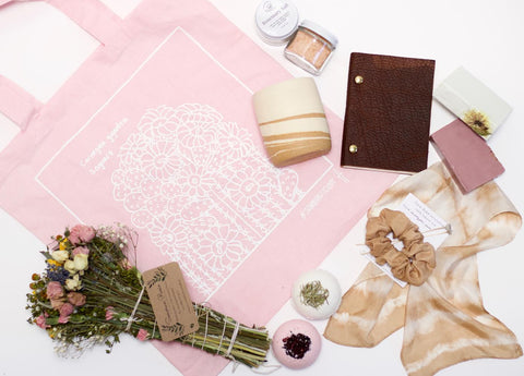 Screenprinted pink tote bag and bouquet of flowers, bath bombs, ceramic mug and natural plant dyed scarf arranged on the ground