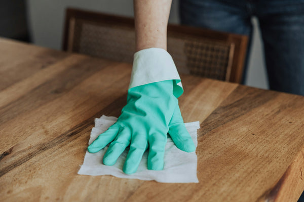 A person cleaning a wooden table with a green glove photo