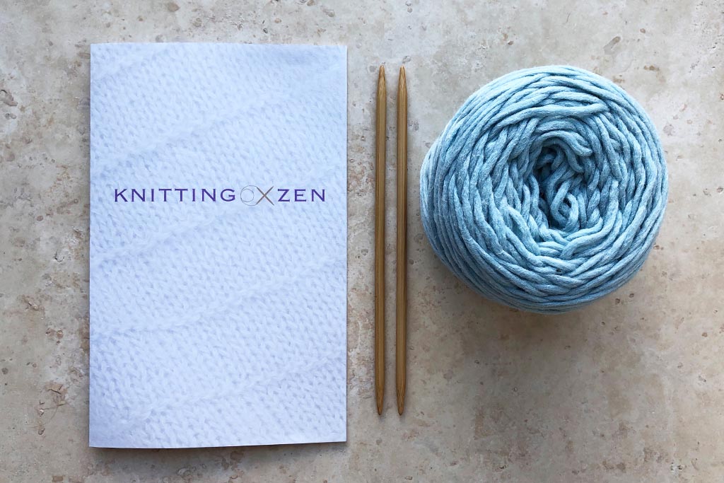 Guidebook, knitting needles and a ball of yarn on a marble surface