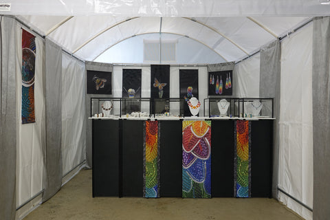 a white tent with banners and jewelry displays in bright colors.