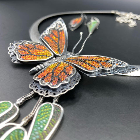 close up of micro-mosaic monarch butterfly pendant with dangling eucalyptus leaves, butterfly is three-dimensional with antennae and a furry carved and forged silver body.