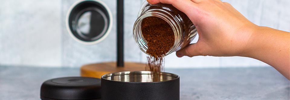 Pouring ground coffee from a mason jar into an airtight storage container