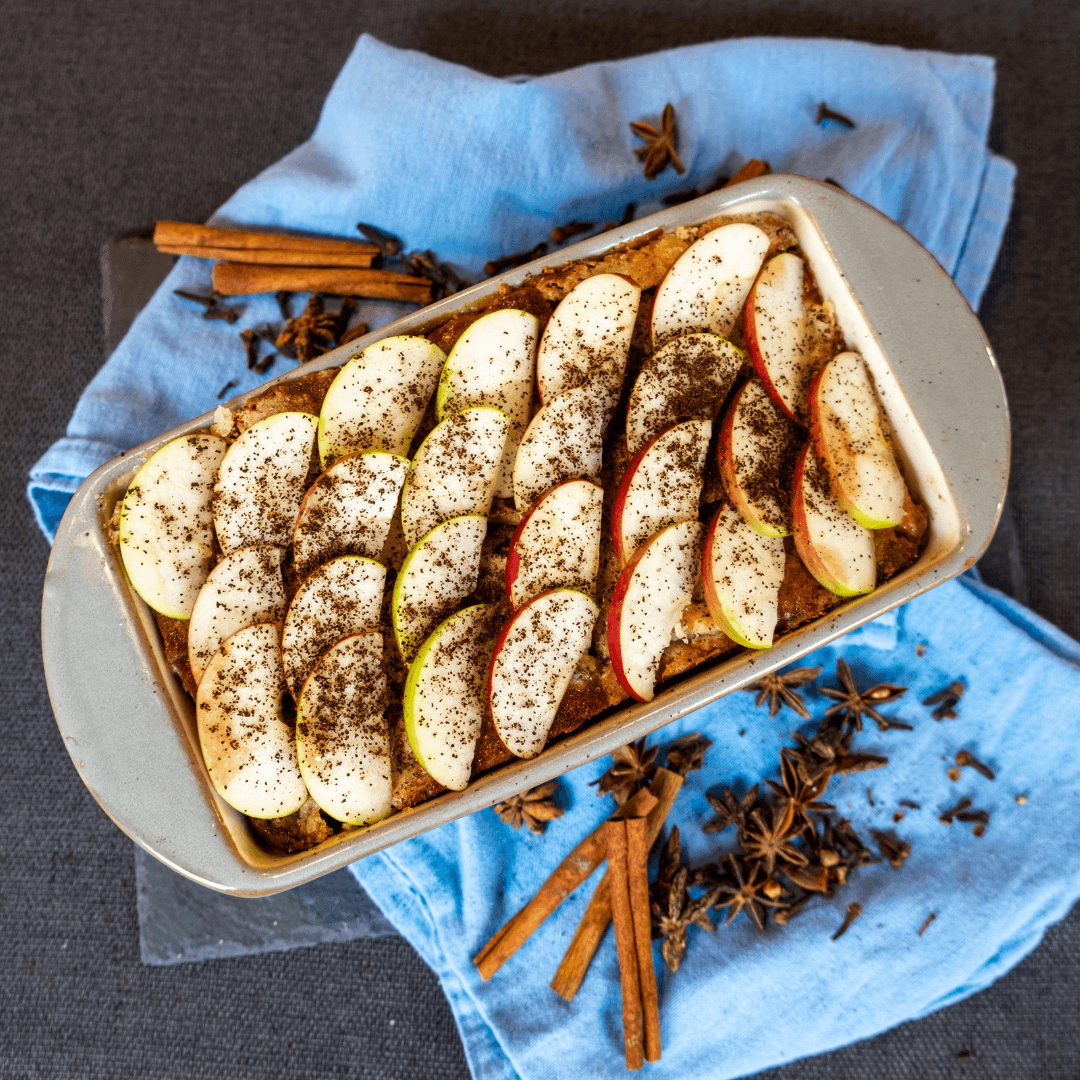 The easy apple coffee cake recipe is finished and presented in a large pan, sitting on a blue towel with cinnamon and other spices beside it