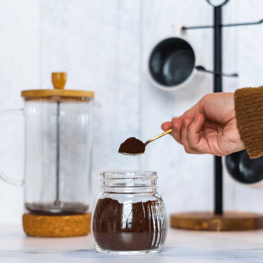 In the kitchen, ground coffee that was stored in a glass mason jar is being scooped out to put in a French press