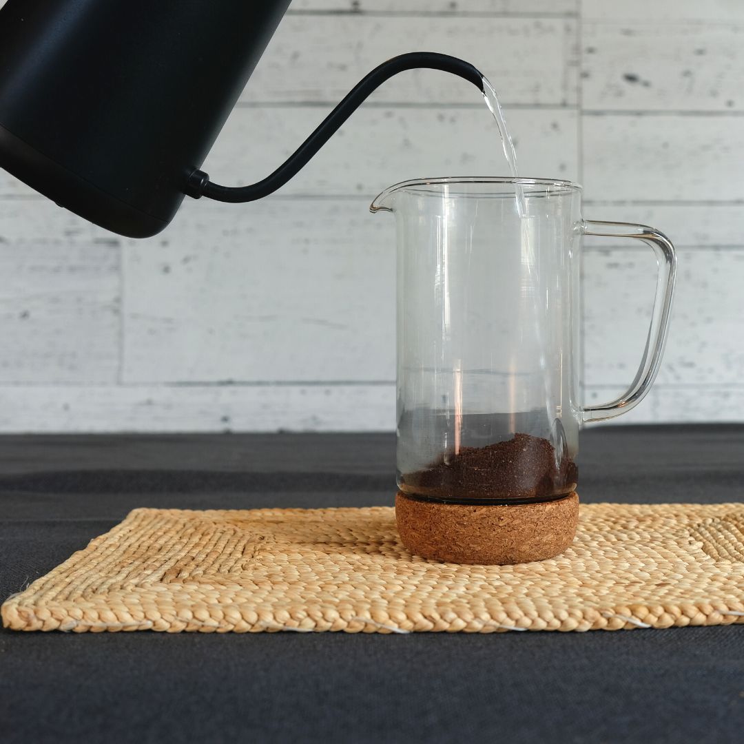 Pouring hot water from a kettle onto coffee grounds in a French press on a counter