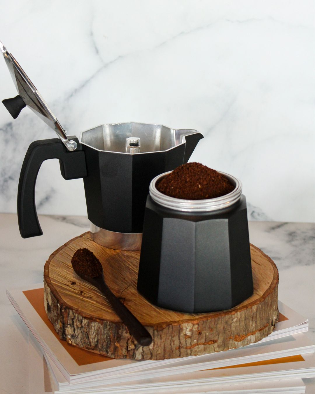 A moka pot sits open, with coffee grounds added to the chamber