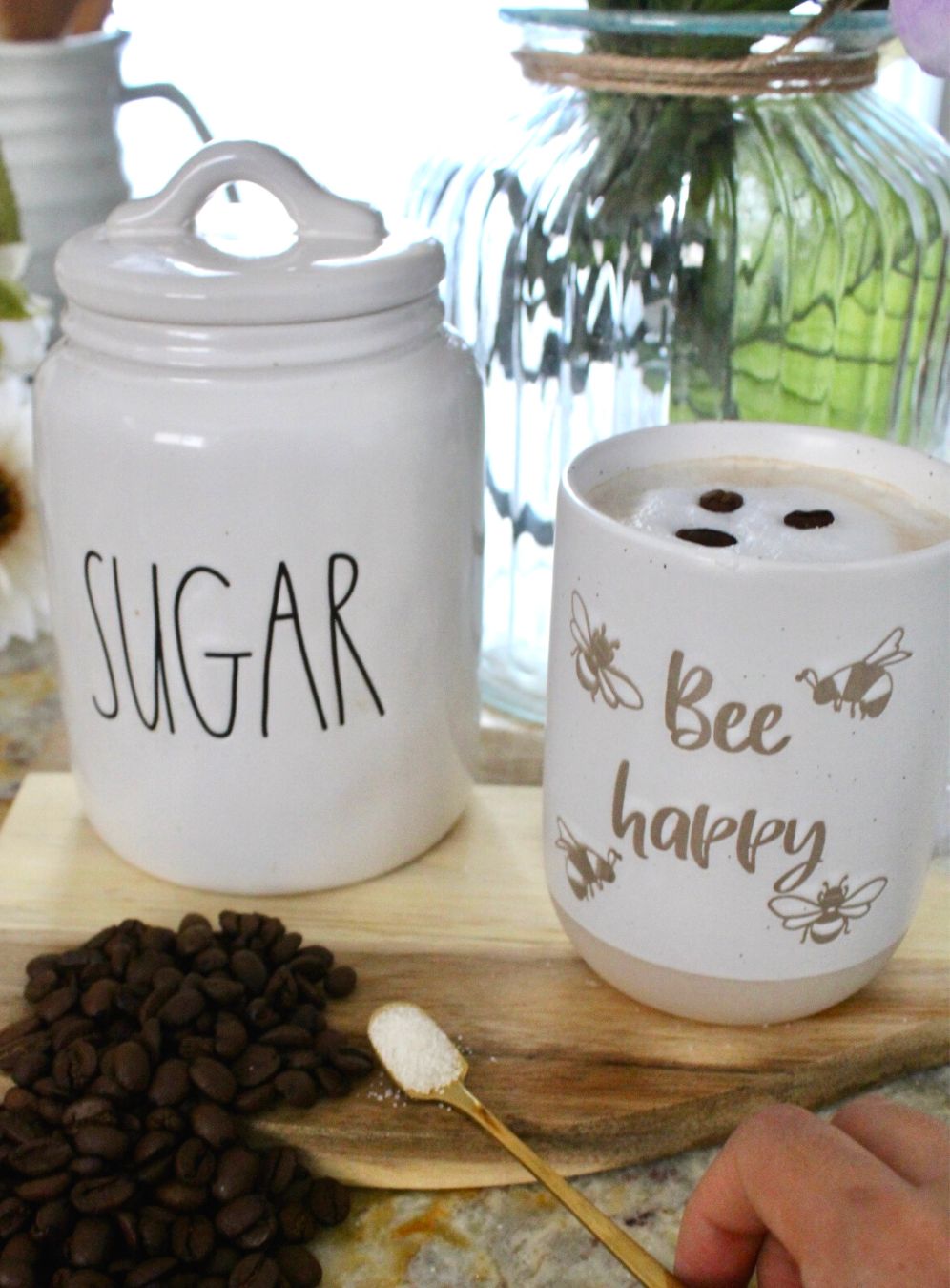 A jar of sugar and a cup of coffee sit on a table with coffee beans