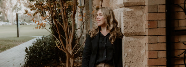 Founder of The 20 Starter Years Planners & Stationery, Angela Shaw, stands in front of the Arts building at the University of Western Australia looking at something out of frame, underneath an autumn tree