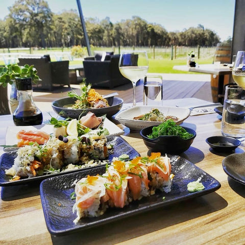 Sushi and wine served at Fishbone Wines on an outdoor table with trees and grass in the background