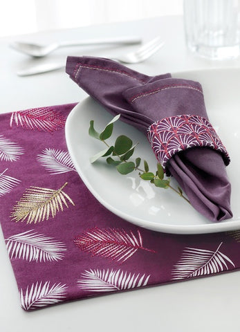 A napkin on a plate on a placemat showing embroidered leaves using metallic thread