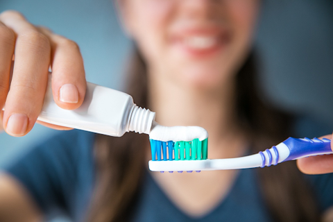 image of a smiling woman applying sensitive toothpaste on a toothbrush