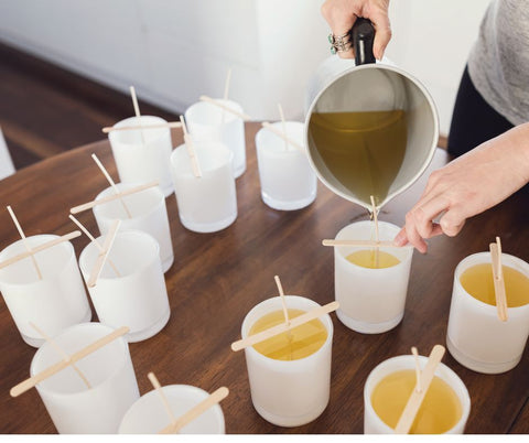 person pouring melted wax into white empty candle jars