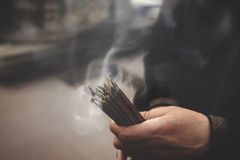 a hand holding a bunch of burning and smoking incense sticks