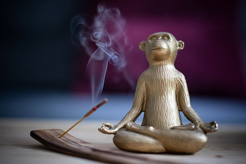 a monkey meditating in a yoga pose while a single incense stick burns with smoke in the air