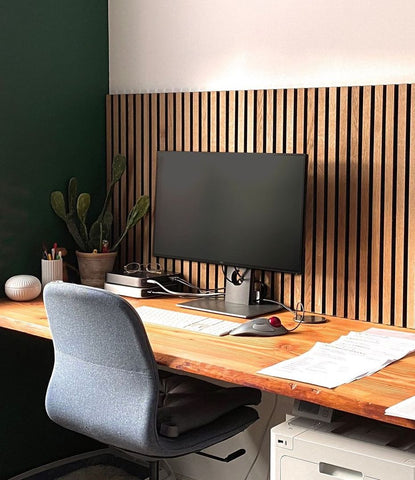home office with decorative sound absorbing wood slat wall panels in front of wood desk and chair with black computer monitor