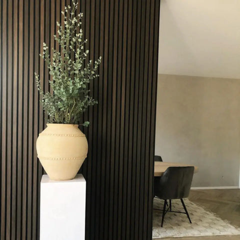 Elegant smoked oak wood wall slats behind a potted plant, featuring types of decorative wood wall panels for a modern look