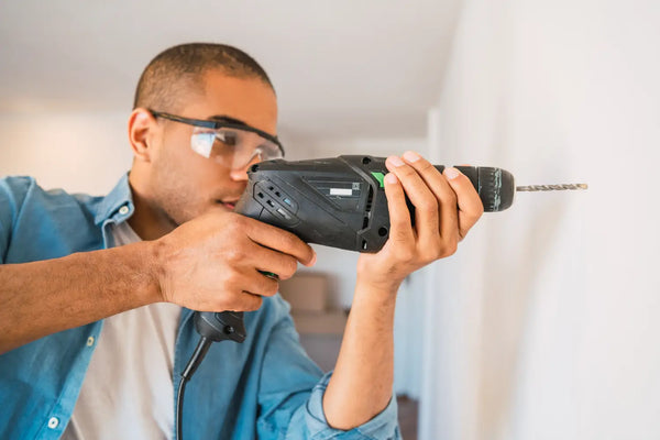 Man drilling into a wall, a step in how to install acoustic panels on wall, wearing protective eyewear