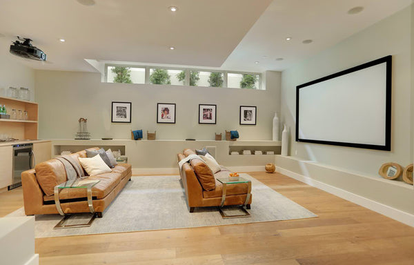 bright modern basement home theater with tan leather couches and a large projector screen